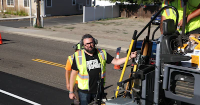 Construction worker in safety vest operating yellow equipment on residential street