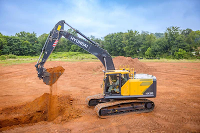 Yellow and black Hyundai excavator digging red soil at a construction site with trees in background