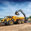 Yellow Hyundai wheel loader and excavator operating at a gravel quarry site with water and trees in background