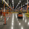 Industrial warehouse with Toyota forklift navigating between red safety barriers and yellow guardrails under bright LED lighting.