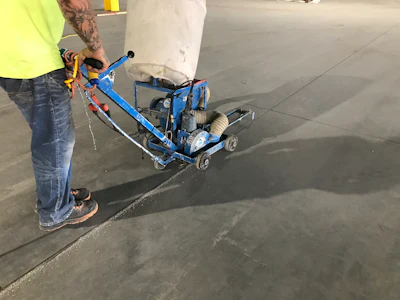 Worker operating blue concrete grinding machine on gray floor surface