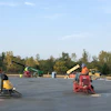 Construction workers operating concrete finishing equipment on a large paved surface with machinery and safety equipment visible in background.