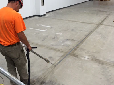 Worker in orange shirt pressure washing concrete floor in industrial facility