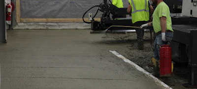 Construction workers in safety vests operating equipment on concrete surface at work site