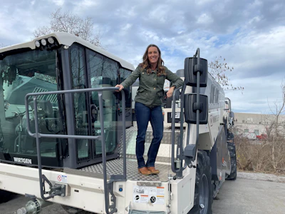Woman posing on Wirtgen industrial truck with tire racks and bare landscape in background