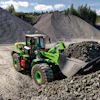Bright green LiuGong wheel loader moving aggregate materials at a quarry with large gravel piles and forested hills in background