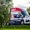 Mack truck with patriotic Heart of Freedom livery featuring American flag design on cab, parked in grassy field with trees