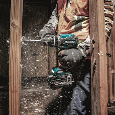Construction worker using Makita cordless drill on wooden door frame with sawdust flying