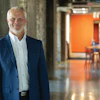 Professional businessman in blue blazer standing in modern office corridor with orange accent wall