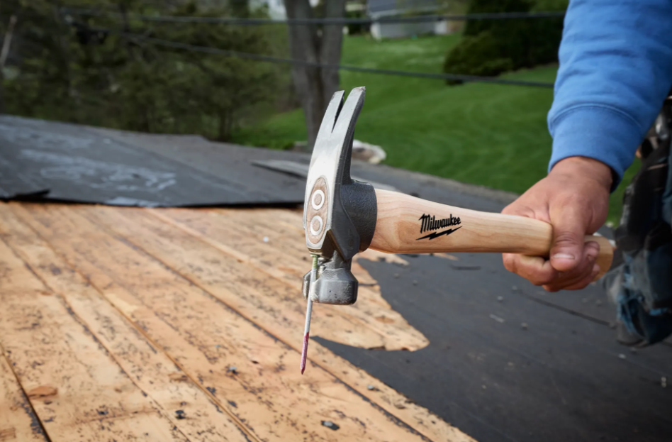 Milwaukee claw hammer with wooden handle being used on roof shingles during construction work