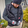 Worker wearing black Milwaukee branded vest and gloves standing near ladder and garden plants