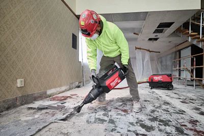 Construction worker in safety gear operating a jackhammer during interior demolition work