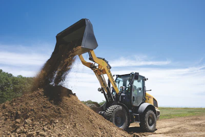 Yellow wheel loader dumping soil at a construction site under clear blue sky
