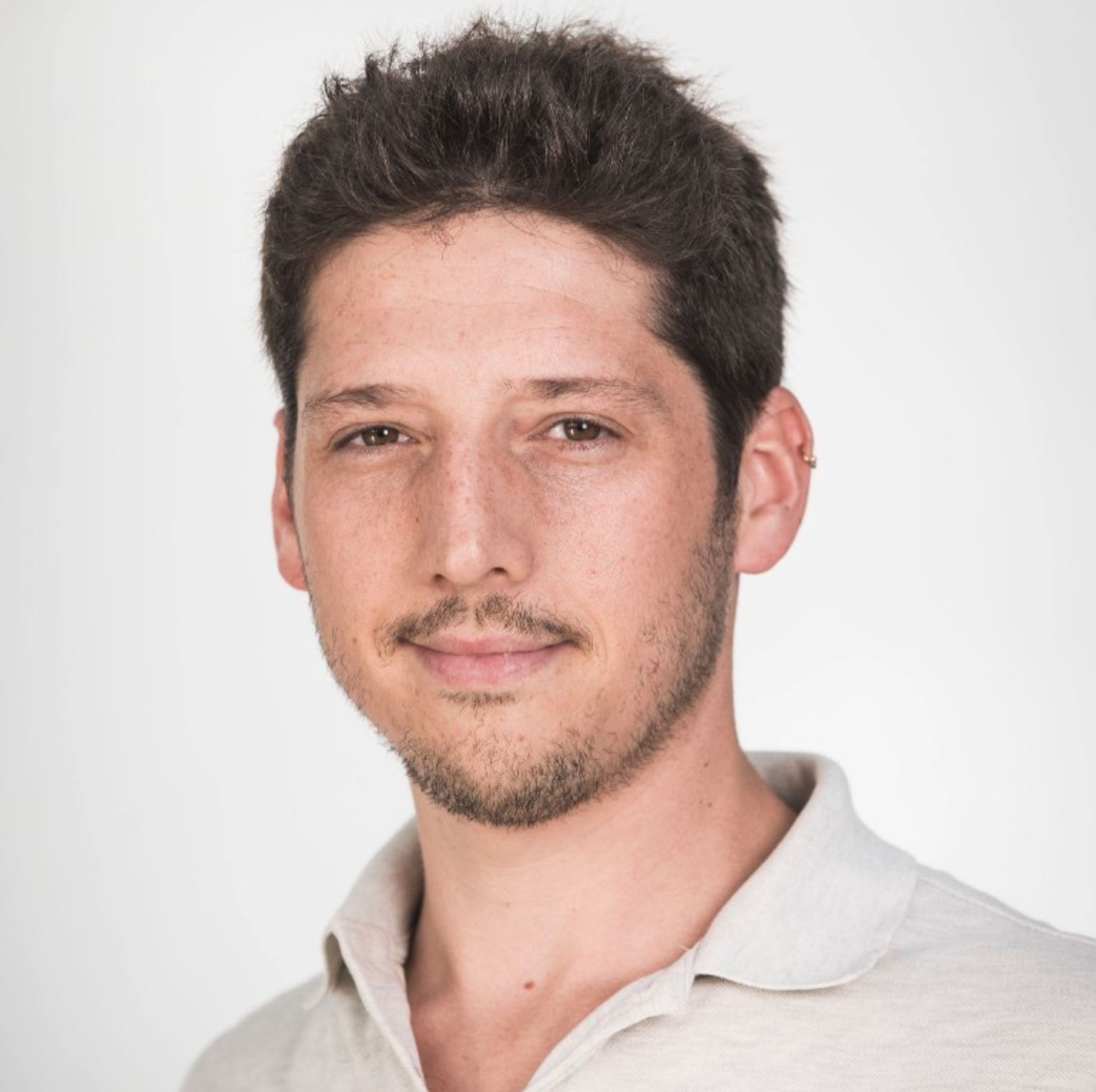 Professional headshot of a man with dark hair and facial hair wearing a light-colored collared shirt against a neutral background Headshot