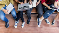 Group of young people sitting together on wooden floor collaborating with laptop and mobile devices