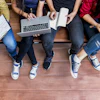 Group of young people sitting together on wooden floor collaborating with laptop and mobile devices