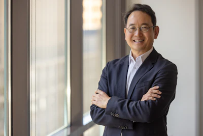Professional man in navy blazer and glasses smiling with arms crossed by office window