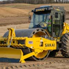 Yellow SAKAI vibratory roller compactor working on construction site with dirt fields in background