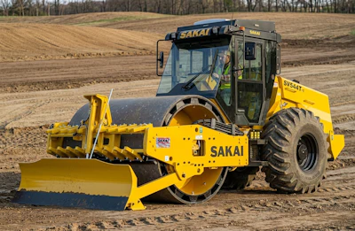 Yellow SAKAI vibratory roller compactor working on construction site with dirt fields in background