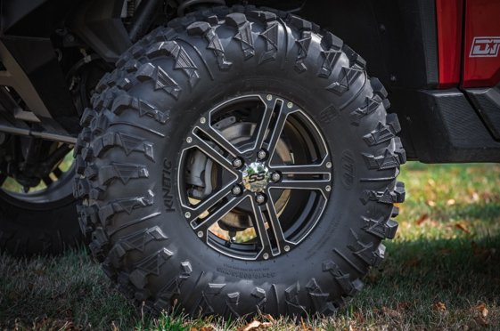 Black all-terrain tire with chrome multi-spoke wheel rim on lifted truck parked on grass