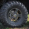 Black all-terrain tire with chrome multi-spoke wheel rim on lifted truck parked on grass