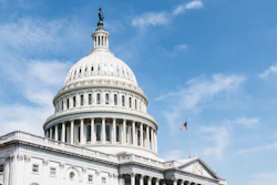U.S. Capitol Building dome with neoclassical architecture and American flag against blue sky