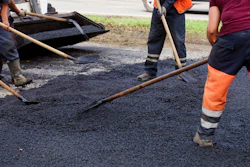 Construction workers laying asphalt on a road using hand tools and spreading equipment