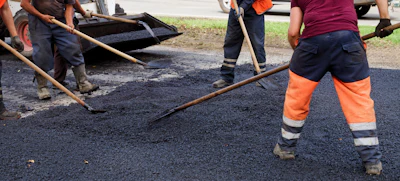 Construction workers laying asphalt on a road using hand tools and spreading equipment