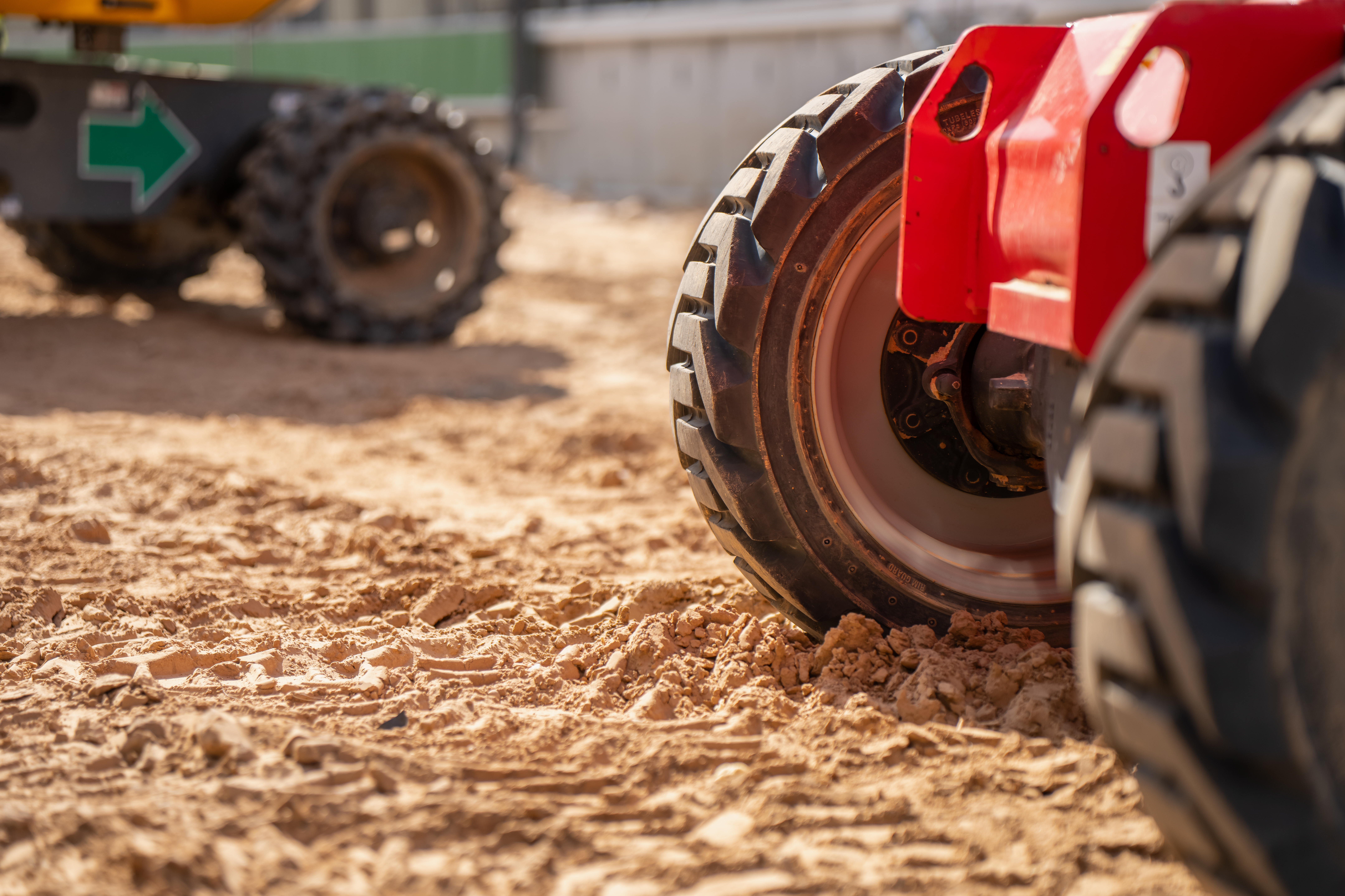 Red construction compactor wheel on sandy work site with heavy machinery in background