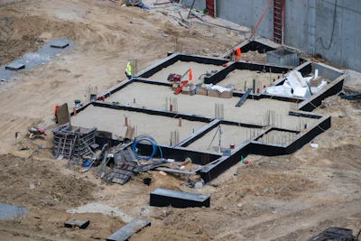 Aerial view of construction site foundation with concrete forms, rebar, and workers in safety equipment