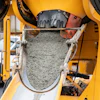 Yellow concrete mixer truck with rotating drum filled with wet gray concrete at job site