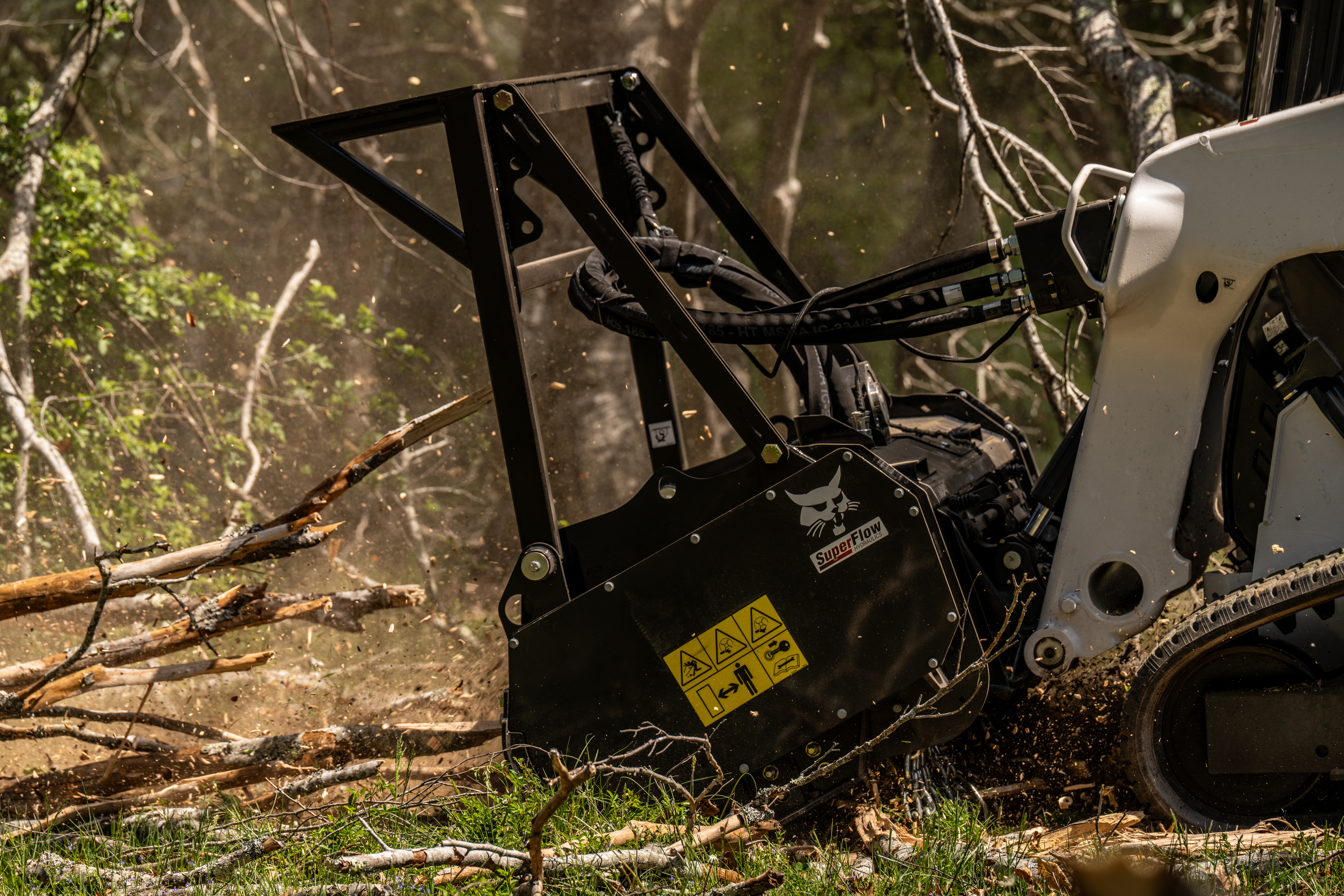 Black snow blower with yellow warning label clearing branches in forest setting