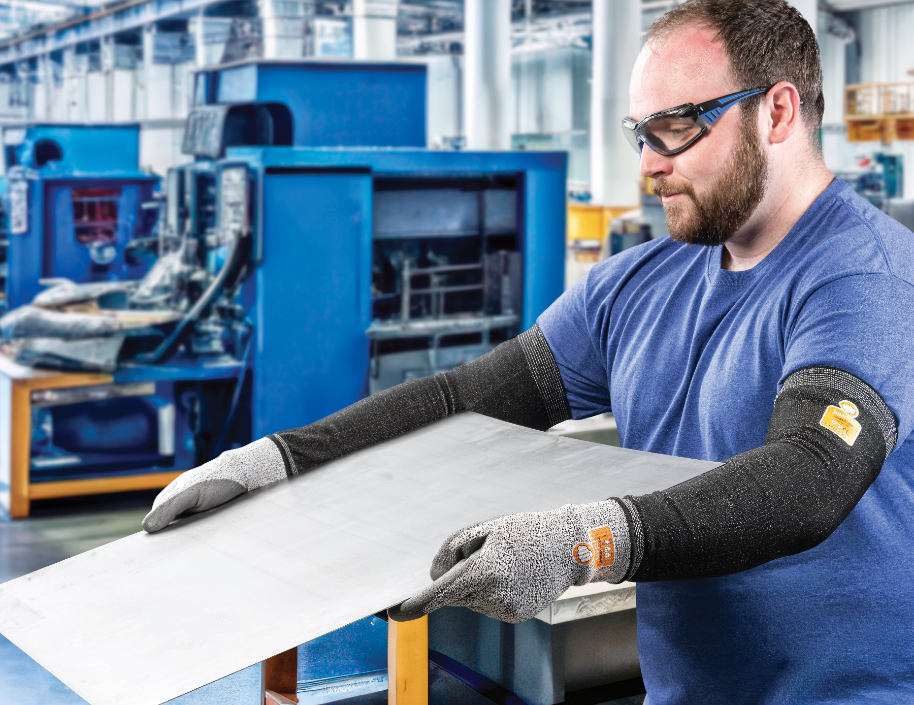 Factory worker wearing safety glasses and protective gloves inspects material at workstation in industrial manufacturing facility