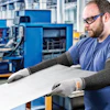 Factory worker wearing safety glasses and protective gloves inspects material at workstation in industrial manufacturing facility