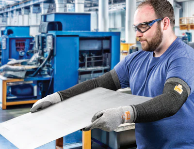 Factory worker wearing safety glasses and protective gloves inspects material at workstation in industrial manufacturing facility