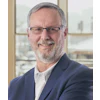 Professional headshot of a bearded man wearing glasses and navy blazer in modern office setting