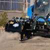 Blue industrial truck with black attachment equipment creating dust clouds at a construction site