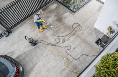 Aerial view of two workers pressure washing a concrete patio with equipment and hoses