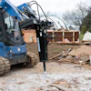 Blue skid steer loader with hydraulic jackhammer attachment at demolition site with debris