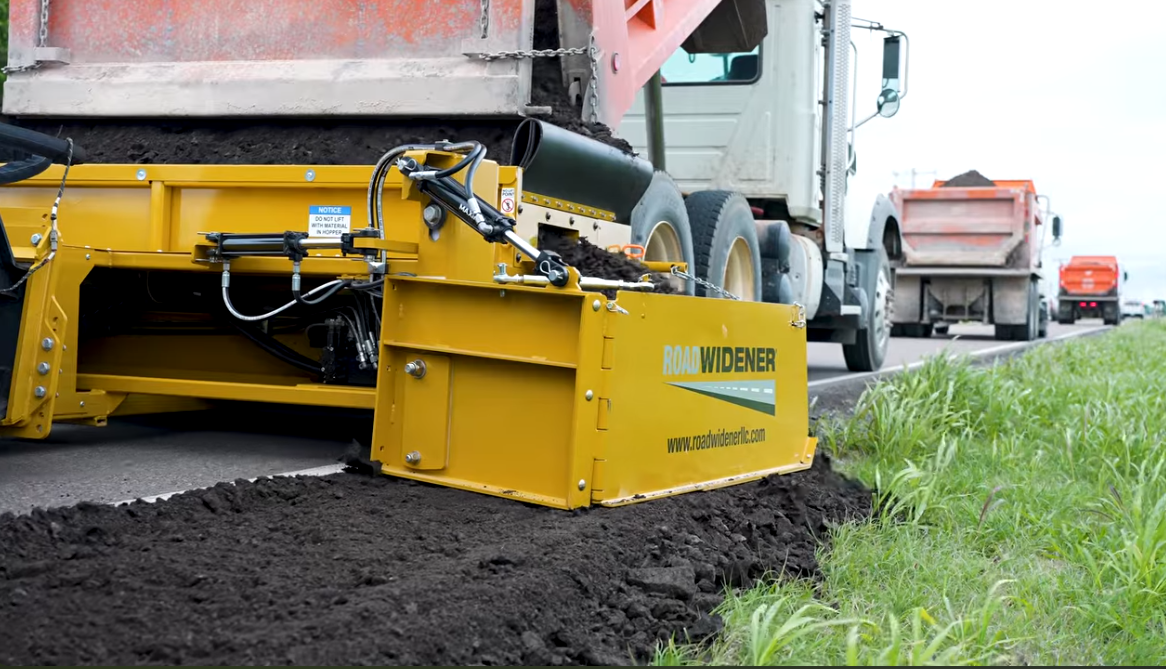 Yellow Widener asphalt paver machine laying dark asphalt on a road with construction trucks in background