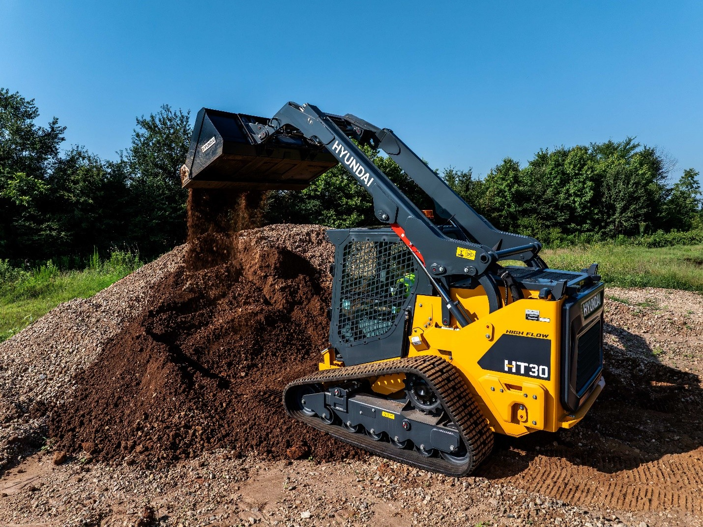 Hyundai HT30 compact track loader dumping gravel at a construction site with trees in background
