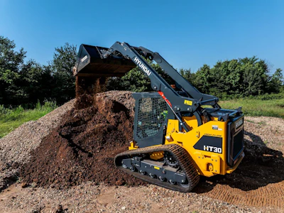 Hyundai HT30 compact track loader dumping gravel at a construction site with trees in background