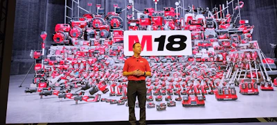 Speaker presenting M18 power tools display at corporate event with hundreds of red tools backdrop