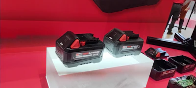 Milwaukee M18 lithium-ion battery packs displayed on white platform with red background