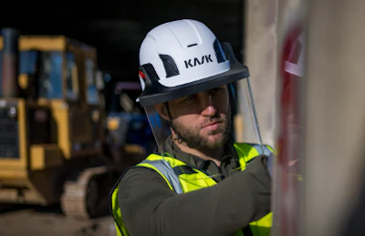 Construction worker wearing white KASK safety helmet with yellow-green reflective vest on industrial job site