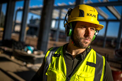 Construction worker wearing yellow KASK safety helmet and neon green reflective vest at industrial building site
