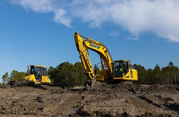 Yellow Komatsu excavator and bulldozer on construction site with dirt mound and forest background