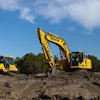 Yellow Komatsu excavator and bulldozer on construction site with dirt mound and forest background
