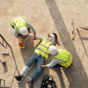 Two construction workers in safety vests and hard hats reviewing plans at a job site