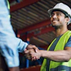 Construction workers in safety gear shaking hands at a warehouse site